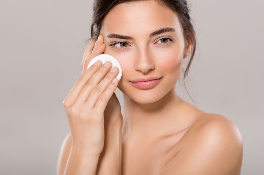 65157888 - healthy fresh girl removing makeup from her face with cotton pad. beauty woman cleaning her face with cotton swab pad isolated on grey background. skin care and beauty concept.
